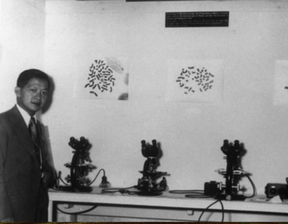 Black and white photo of man standing next to row of microscopes